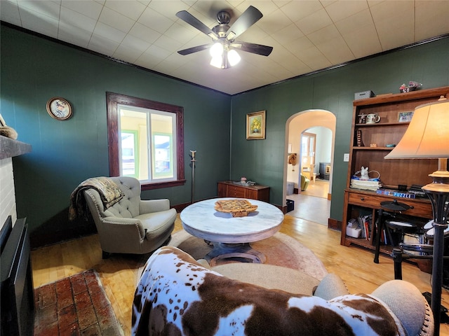 living area with arched walkways, a ceiling fan, crown molding, and light wood-type flooring