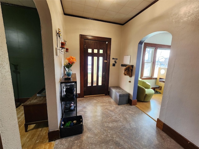 foyer with baseboards, a textured wall, arched walkways, and ornamental molding