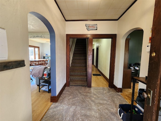 hallway with arched walkways, crown molding, baseboards, and wood finished floors