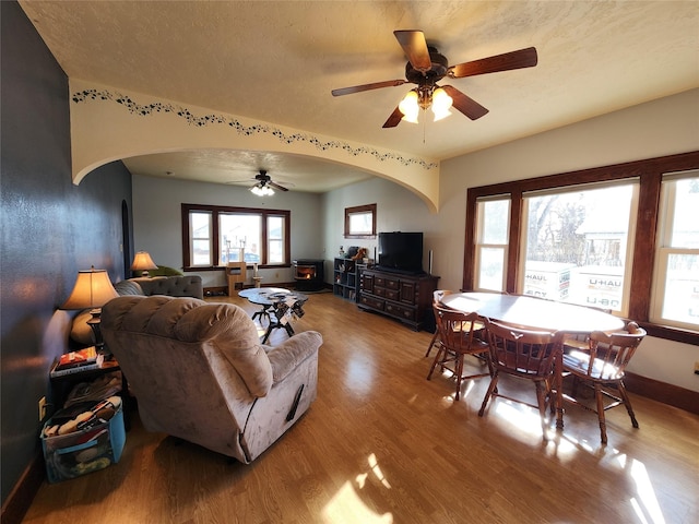 living room featuring arched walkways, ceiling fan, baseboards, and light wood finished floors