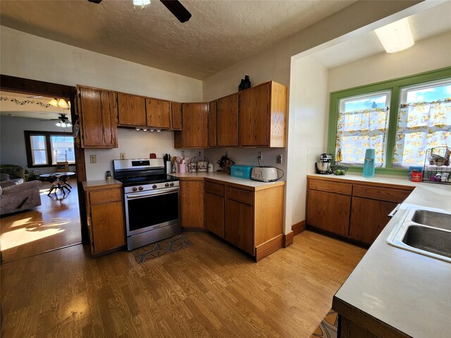kitchen with light countertops, wood finished floors, brown cabinetry, electric stove, and ceiling fan