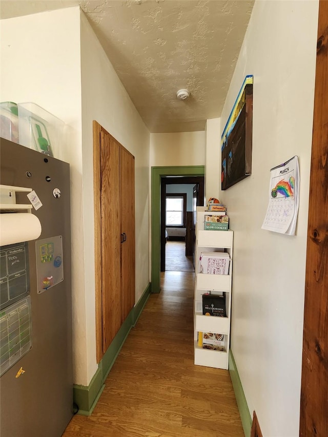 hallway featuring baseboards, wood finished floors, and a textured ceiling