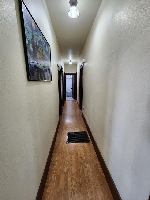 corridor with wood finished floors, baseboards, and visible vents