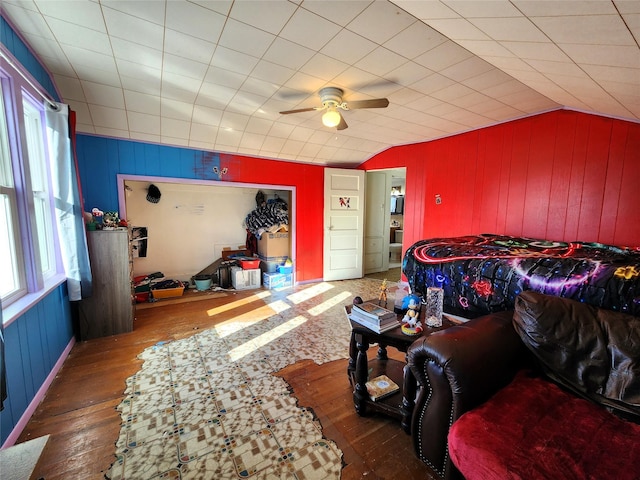 living room featuring lofted ceiling, wooden walls, a ceiling fan, and wood-type flooring