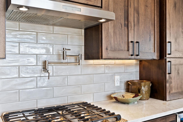 85 Meadows Dr, Whitefish, MT 59937 - kitchen view of range hood, decorative backsplash, pot filler, dark brown cabinetry, and light stone counters