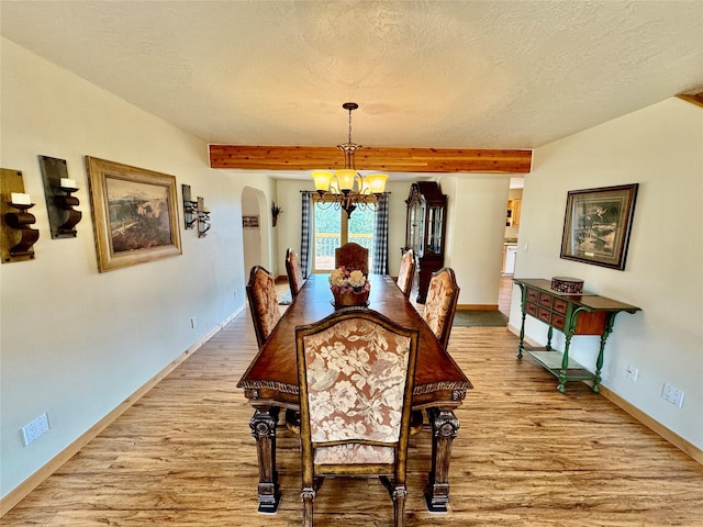 19066 King Rd, Florence, MT 59833 - dining room with a chandelier, light wood-style floors, a textured ceiling, beamed ceiling, and arched walkways