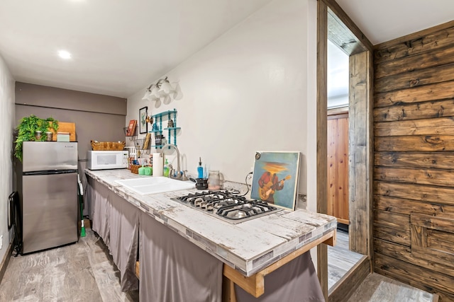 kitchen with a sink, tile counters, appliances with stainless steel finishes, and light wood-type flooring