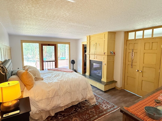 675 Bobcat Ln, Hamilton, MT 59840 - bedroom with access to exterior, baseboards, dark wood-style floors, a textured ceiling, and a multi sided fireplace