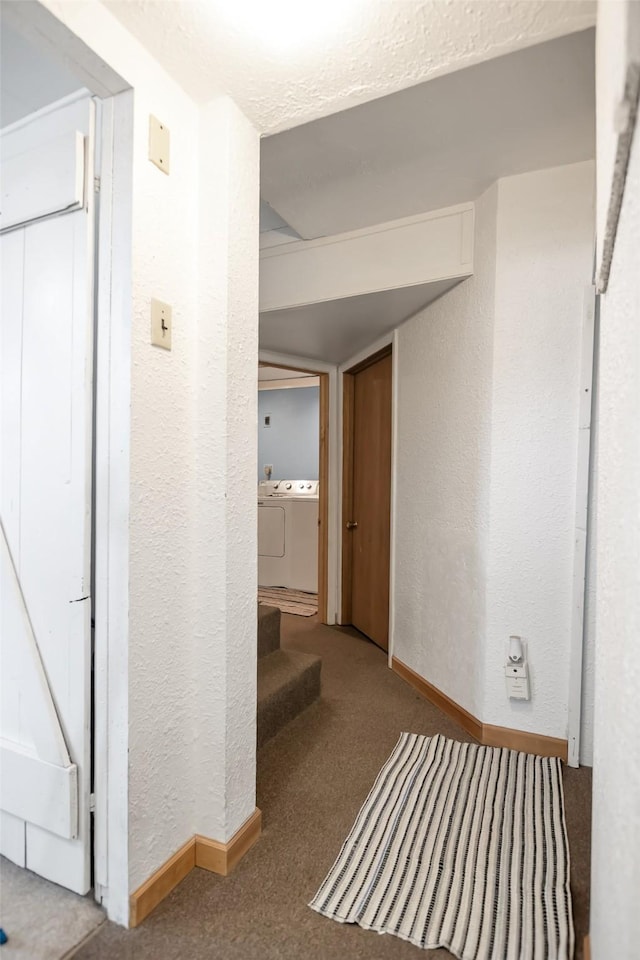 hall featuring independent washer and dryer, a textured wall, carpet, baseboards, and a textured ceiling