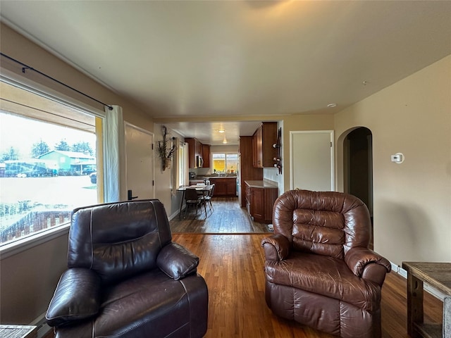 living area featuring arched walkways, baseboards, and dark wood-type flooring