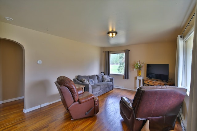 living room featuring arched walkways, baseboards, wood finished floors, and a baseboard heating unit