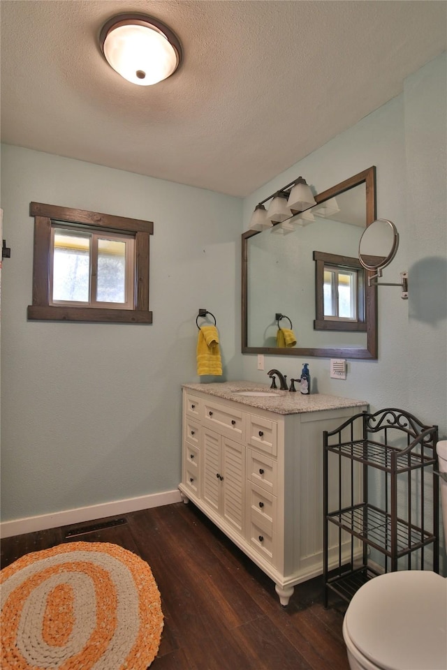 bathroom with a textured ceiling, baseboards, toilet, wood finished floors, and vanity