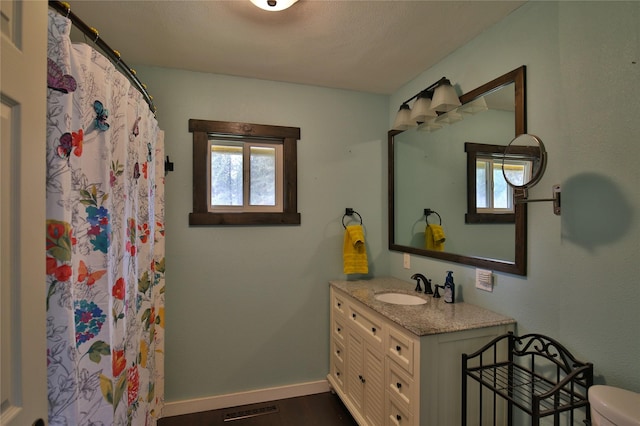 bathroom with vanity, toilet, baseboards, visible vents, and wood finished floors