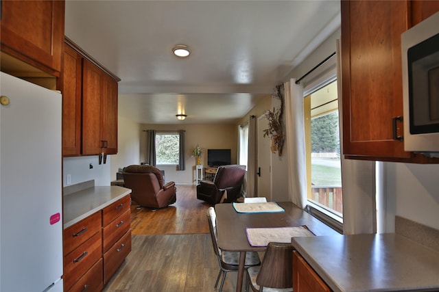 kitchen with open floor plan, stainless steel microwave, dark wood finished floors, freestanding refrigerator, and brown cabinetry
