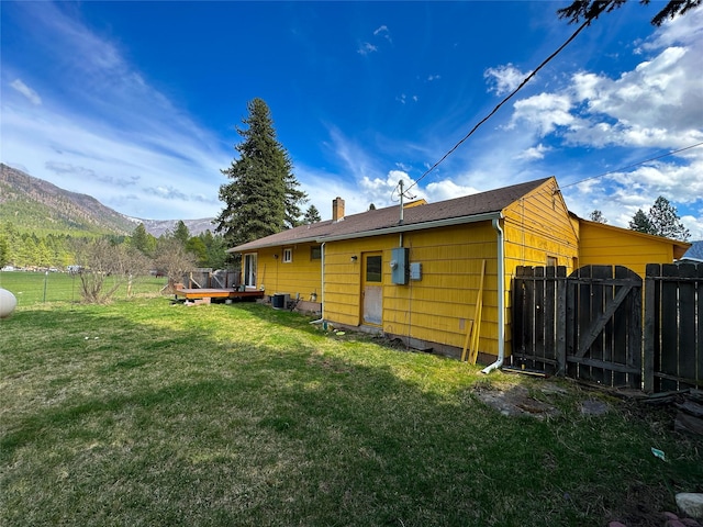 rear view of house with a chimney, fence, a gate, a deck with mountain view, and a lawn