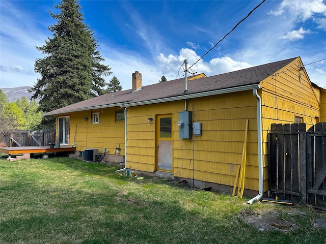 back of house featuring a yard, central AC unit, fence, and a chimney
