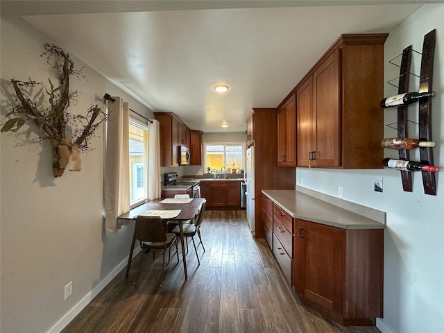 kitchen with dark wood-style floors, brown cabinetry, baseboards, and stainless steel appliances