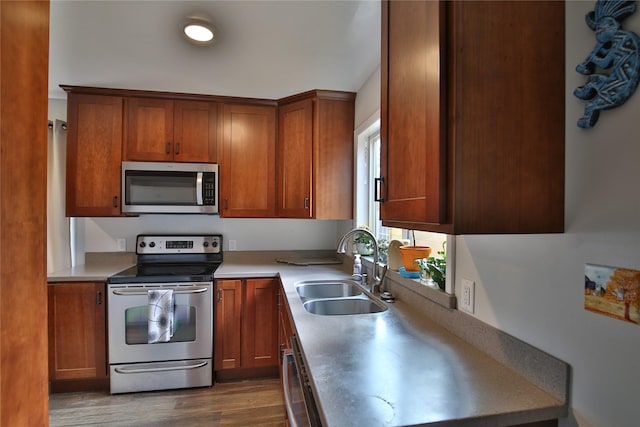 kitchen featuring light countertops, dark wood-type flooring, a sink, appliances with stainless steel finishes, and brown cabinets