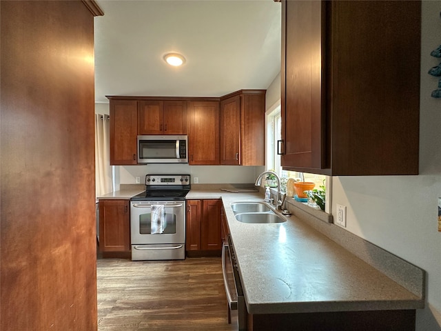 kitchen with light countertops, dark wood-style flooring, a sink, appliances with stainless steel finishes, and brown cabinets
