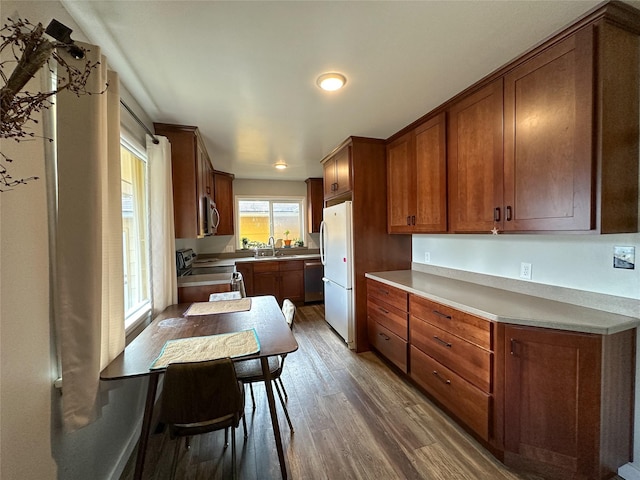 kitchen with light countertops, wood finished floors, stainless steel appliances, a sink, and brown cabinetry