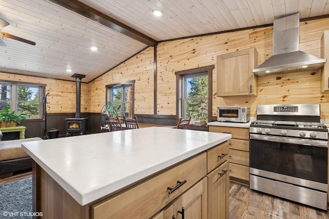 kitchen featuring stainless steel gas range, island exhaust hood, wooden walls, and a wood stove