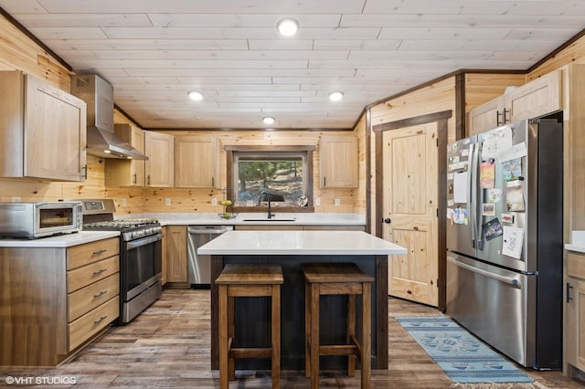 kitchen with light countertops, stainless steel appliances, a sink, wall chimney range hood, and light brown cabinetry
