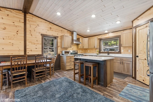 kitchen with a sink, vaulted ceiling with beams, wood finished floors, stainless steel gas range oven, and wall chimney range hood