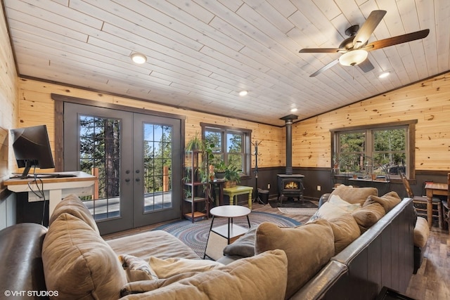 living room with french doors, wooden walls, wood finished floors, a wood stove, and lofted ceiling
