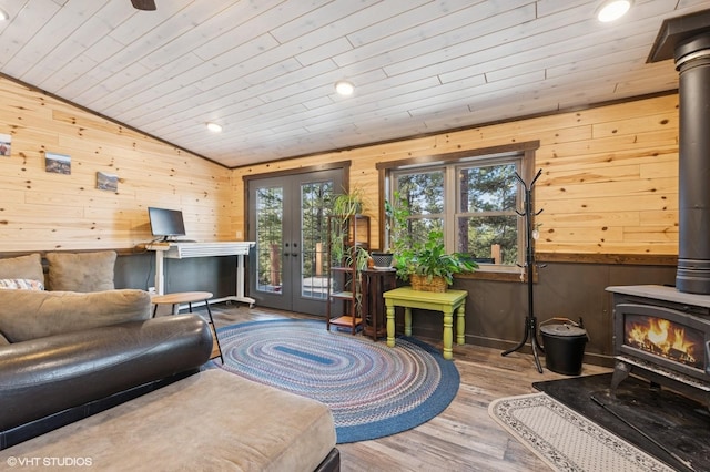 living area featuring wood walls, wood finished floors, lofted ceiling, a wood stove, and french doors