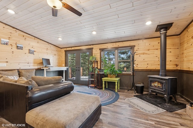 living area with lofted ceiling, wooden walls, wood finished floors, and a wood stove