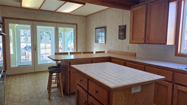 kitchen with brown cabinets, a peninsula, a kitchen bar, and tile countertops
