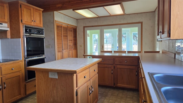 kitchen with dobule oven black, a healthy amount of sunlight, tile countertops, and a sink
