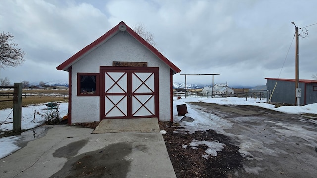 snow covered structure with an outdoor structure, fence, and a storage shed