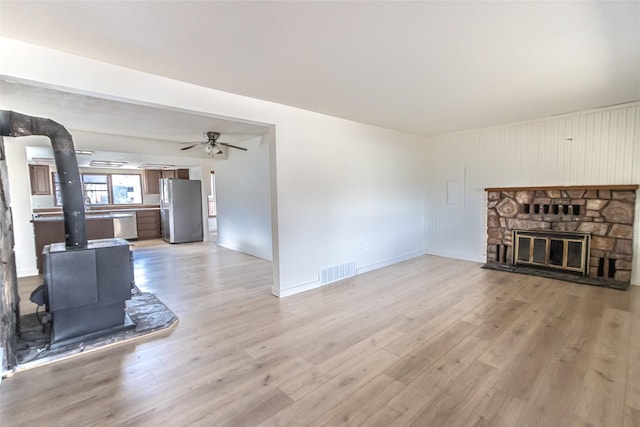 602 16th Ave E, Polson, MT 59860 - unfurnished living room with a wood stove, light wood-style flooring, ceiling fan, baseboards, and a fireplace