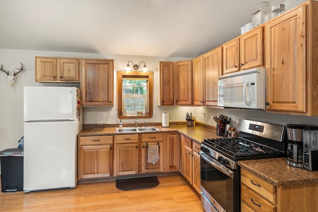 kitchen with a sink, dark countertops, light wood-type flooring, and white appliances