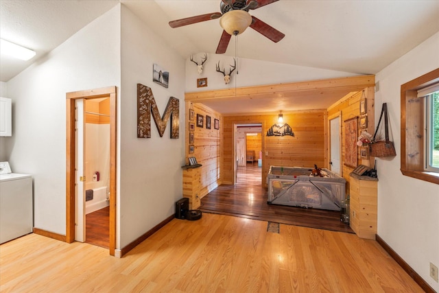 hallway featuring washer / clothes dryer, wood finished floors, vaulted ceiling, and wood walls