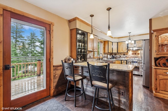 kitchen with a peninsula, a sink, stainless steel appliances, under cabinet range hood, and dark wood finished floors