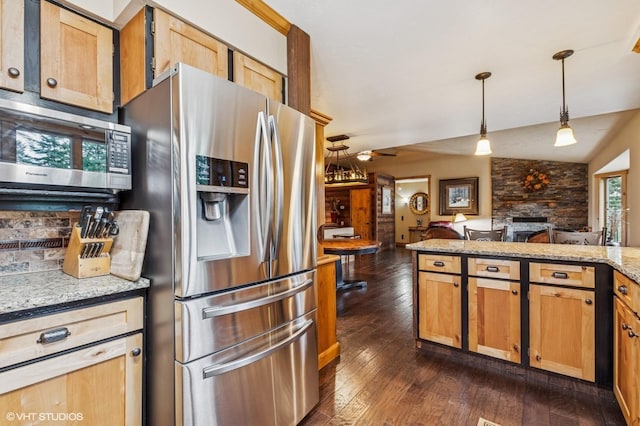 kitchen with appliances with stainless steel finishes, a stone fireplace, dark wood-style floors, decorative light fixtures, and a ceiling fan