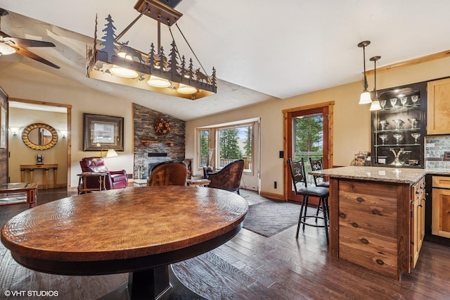 dining room featuring a fireplace, dark wood finished floors, a ceiling fan, vaulted ceiling, and baseboards