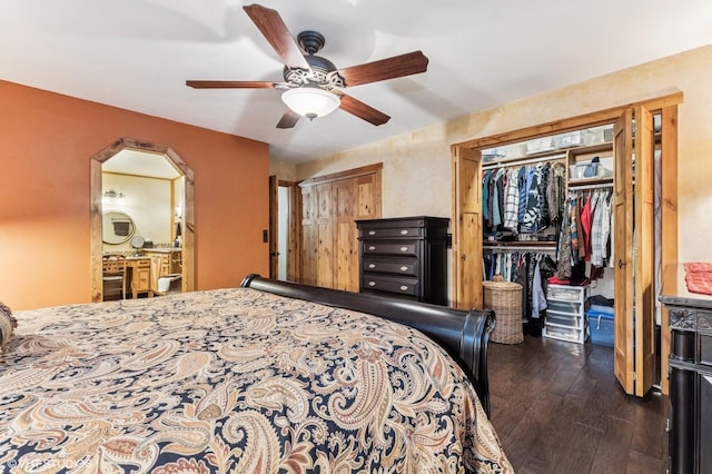 bedroom with dark wood-type flooring, two closets, arched walkways, ceiling fan, and connected bathroom
