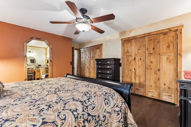 bedroom featuring dark wood-style floors, two closets, arched walkways, ceiling fan, and ensuite bathroom