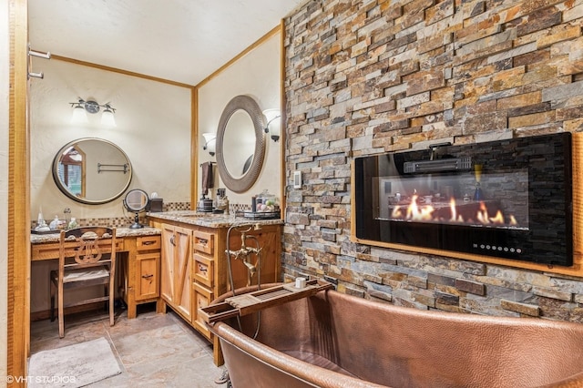 full bathroom with a freestanding bath, vanity, a fireplace, crown molding, and stone finish floors