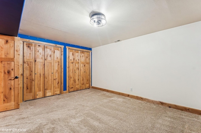 unfurnished bedroom with carpet flooring, two closets, and baseboards