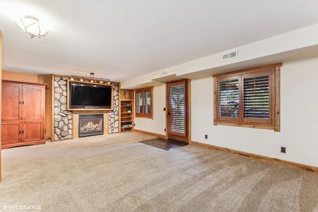 unfurnished living room with carpet, a stone fireplace, and baseboards