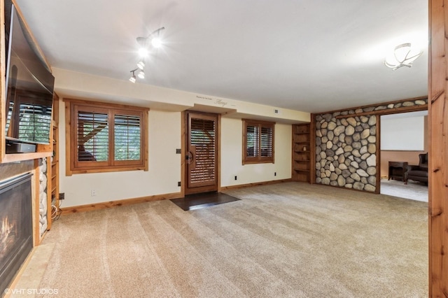 unfurnished living room with a stone fireplace, carpet, and baseboards