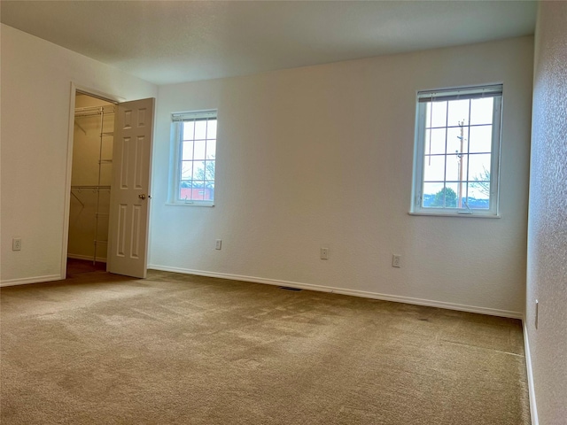 unfurnished bedroom featuring a closet, carpet flooring, a walk in closet, and multiple windows