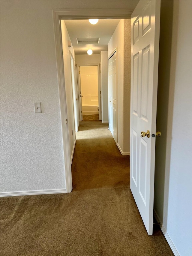 hallway featuring baseboards, a textured wall, and carpet