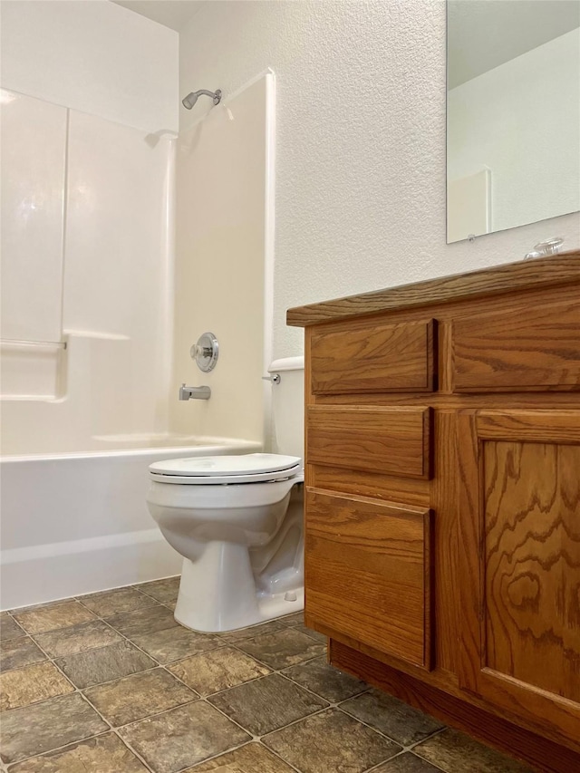 bathroom featuring shower / tub combination, toilet, stone finish flooring, and vanity