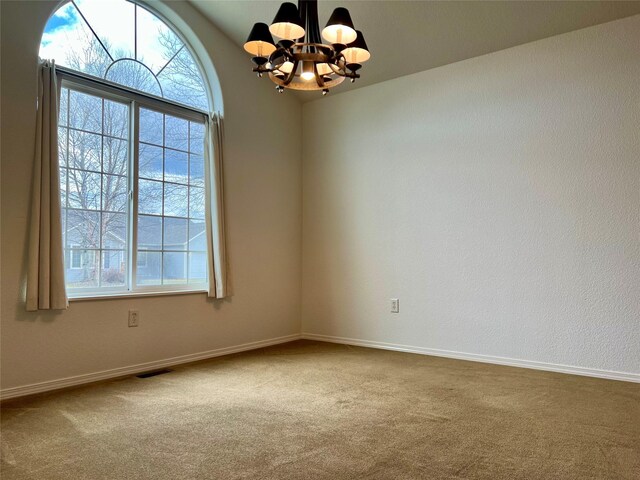 carpeted empty room with baseboards, a notable chandelier, visible vents, and a healthy amount of sunlight