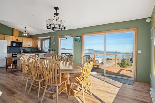 18 Mission View Dr, Polson, MT 59860 - dining space featuring a chandelier, vaulted ceiling, light wood-type flooring, a water view, and a baseboard radiator
